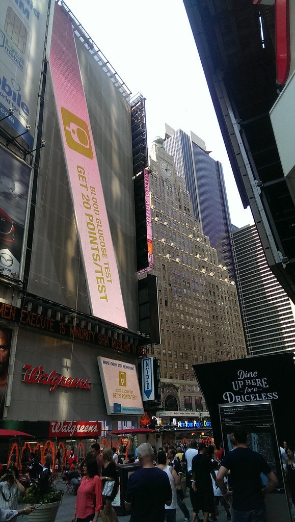 Street soccer players competing on a small pitch in Times Square, New York, surrounded by billboards and spectators.